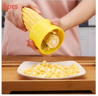 Yellow manual corn thresher kitchen tool with a corn-shaped plastic body and visible stainless steel gear.