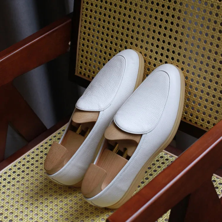 British handmade brown leather men's loafers with a flat TPR sole on a wooden surface.
