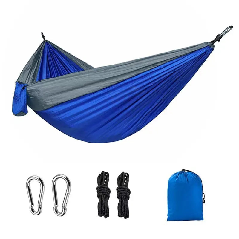 A sapphire blue parachute nylon hammock hung between two trees in a woodland setting.