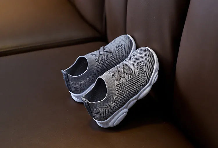 Children's white fabric lazy slip-on shoe with non-slip rubber sole on a wooden floor.
