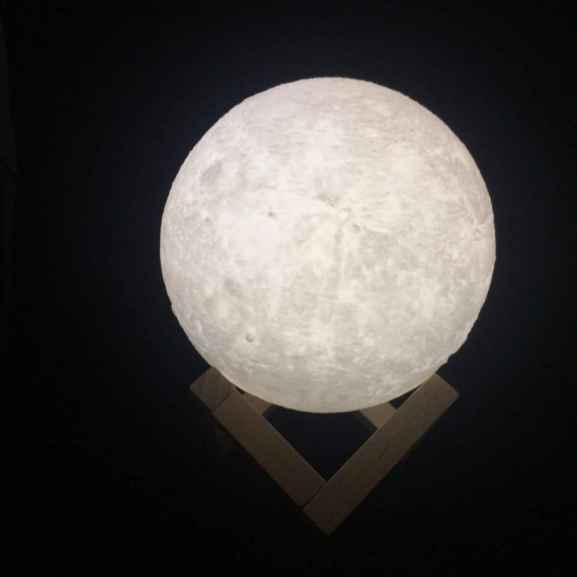 3D printed white moon lamp with detailed lunar surface texture on a wooden holder.