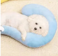 Blue U-shaped cloth pet pillow in a question mark shape on a wooden floor next to a cat carrier.