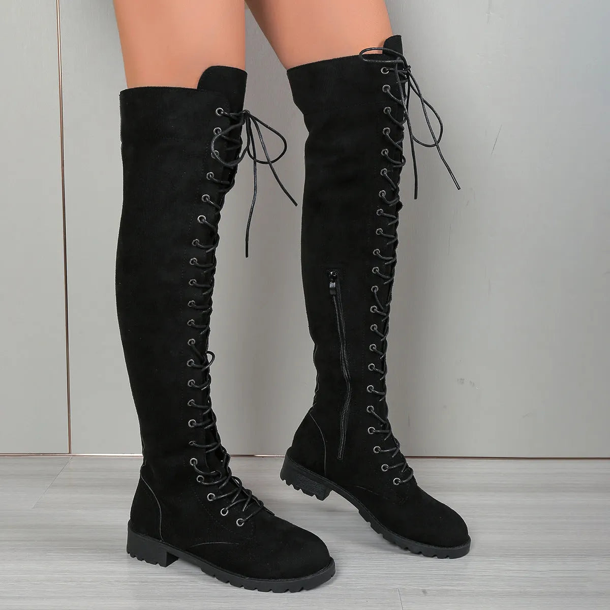 Black lace-up over-the-knee boots with decorative stitching, a round toe, and a flat rubber sole on a neutral background.