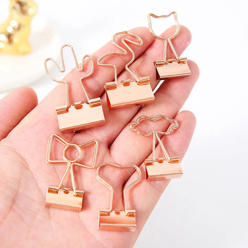 Gold metal paper clip with a long tail, showing decorative flamingo, love, cloud, cat, cactus, and bow motif options.