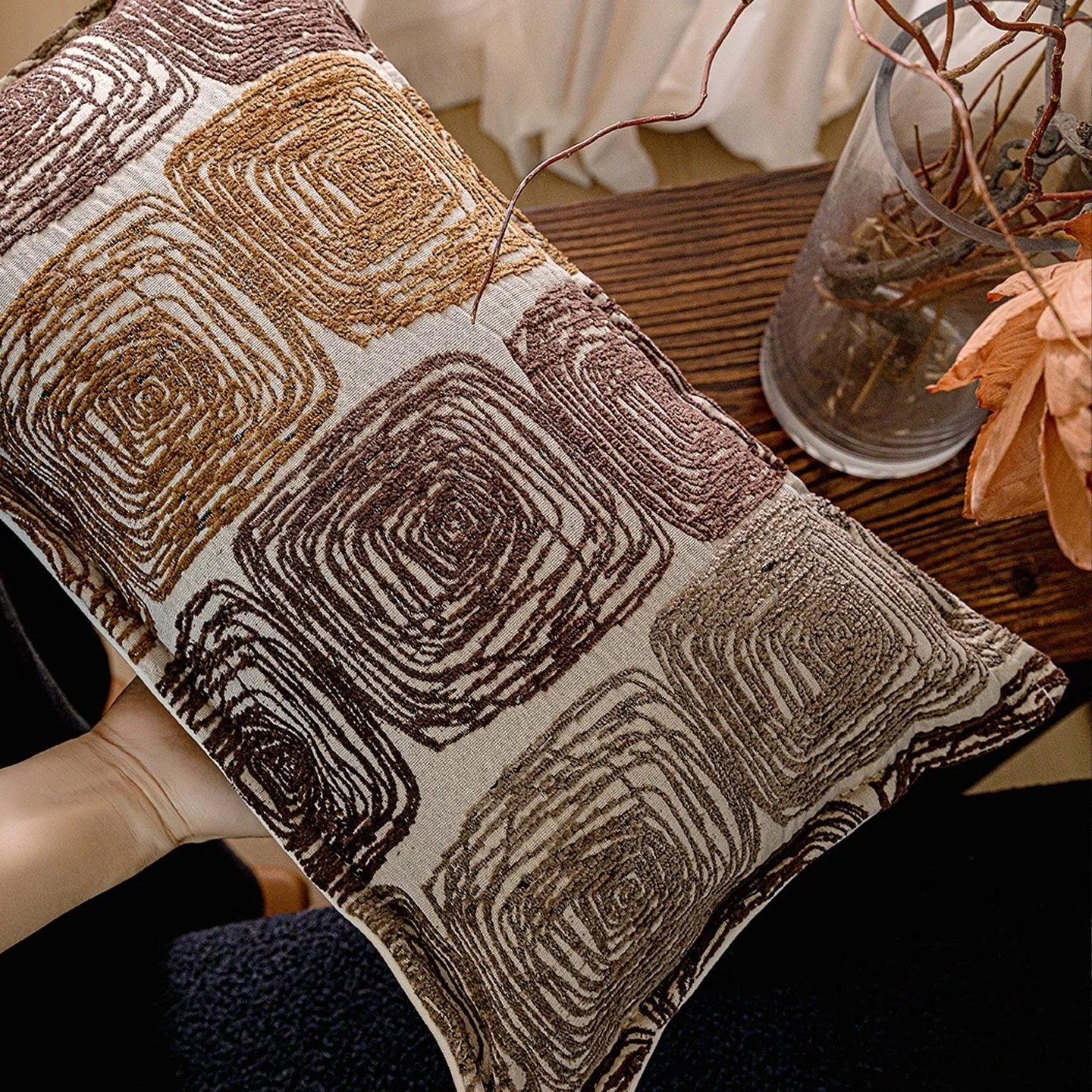 Cream and coffee abstract coil pattern square decorative pillow cover on a grey sofa.