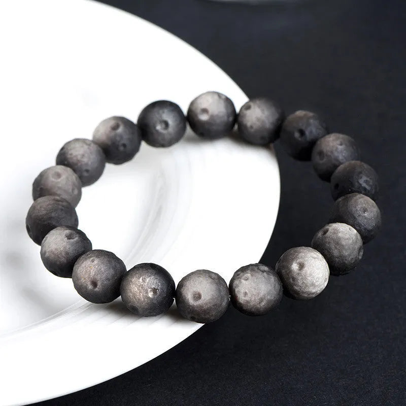 Obsidian crater ball bracelet on a wrist, showing ground stone texture and bead size.