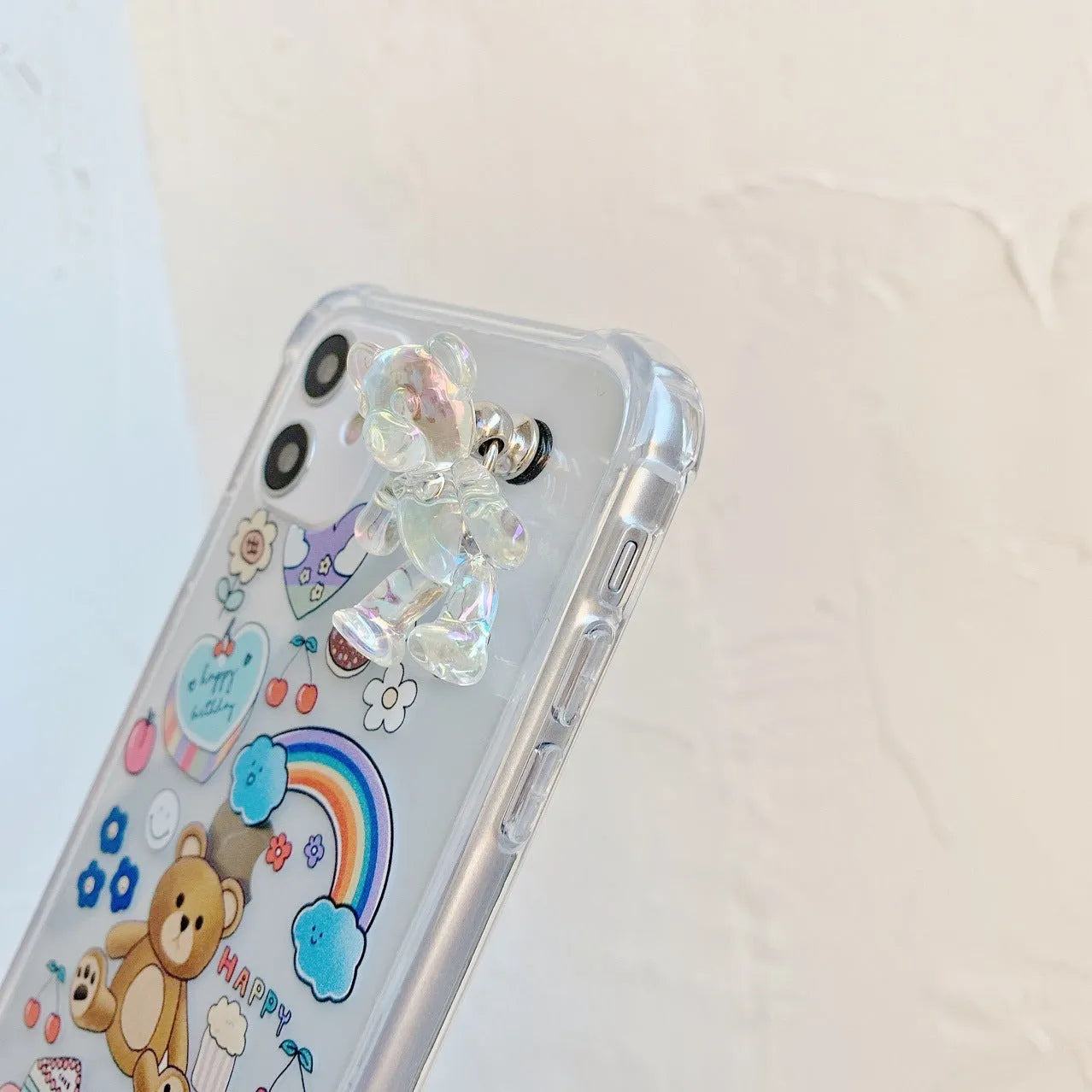 White iPhone case with a cartoon bear design and a connected silver bear pendant on a chain.