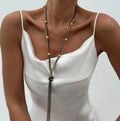 Simple Y-shaped metal tassel necklace in gold finish on a woman, with matching earrings, minimalist style for commuting wear