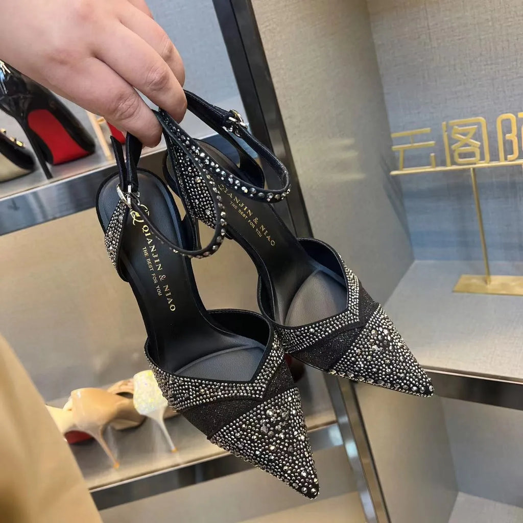 Women's black hollow high heel shoe with red sole, stiletto heel, and pointed toe on a plain background.