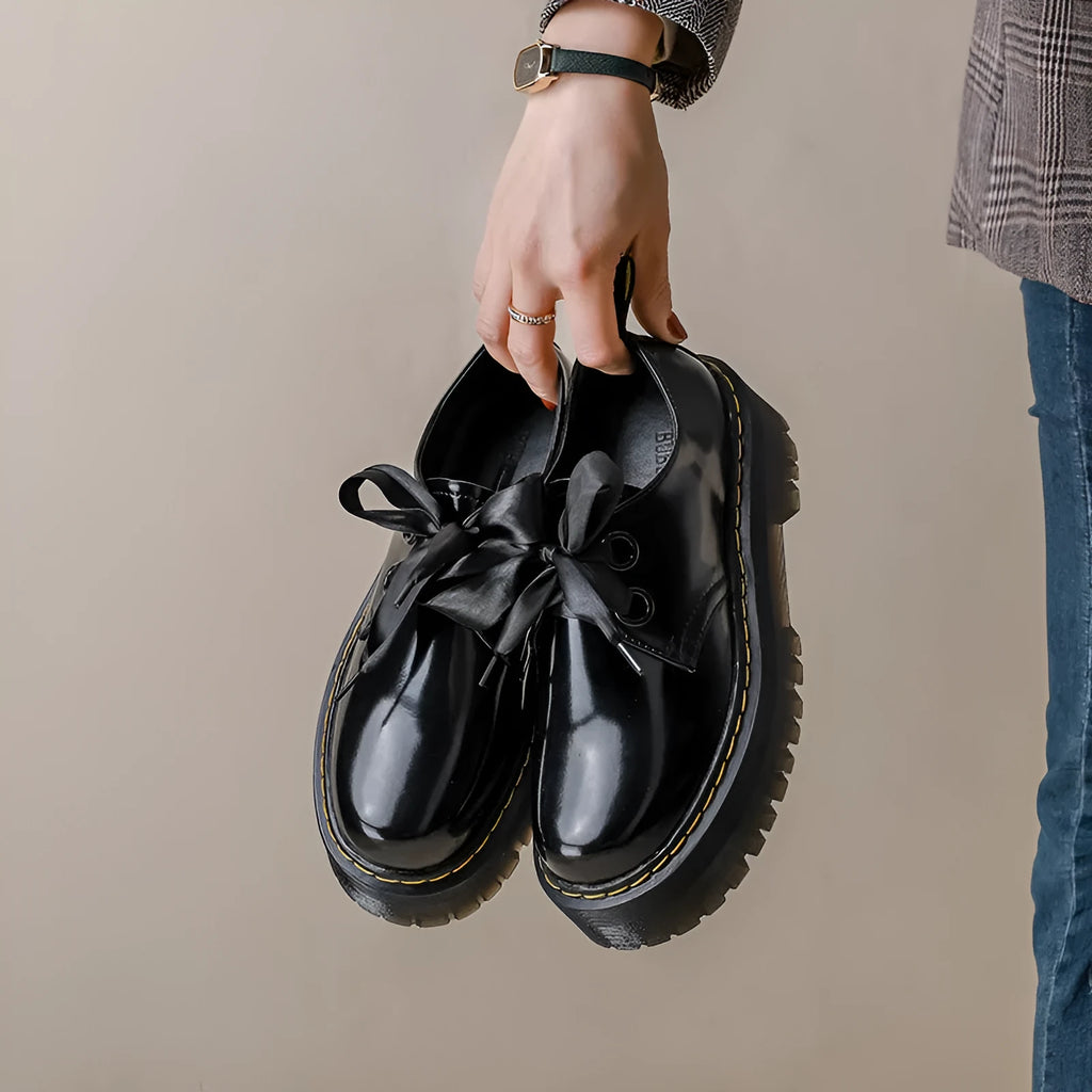 Women's black thick-soled leather shoes with ribbon and cross-strap details on a white background.