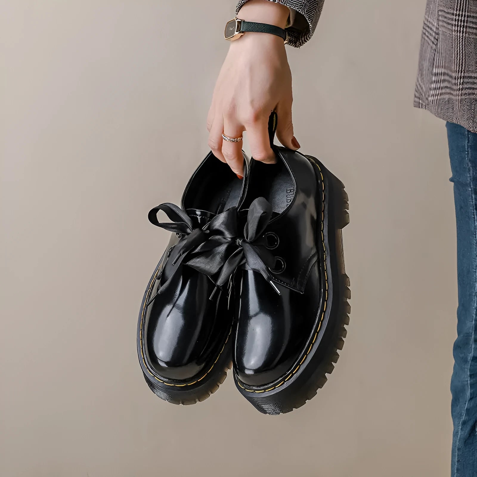Women's black thick-soled leather shoes with ribbon and cross-strap details on a white background.