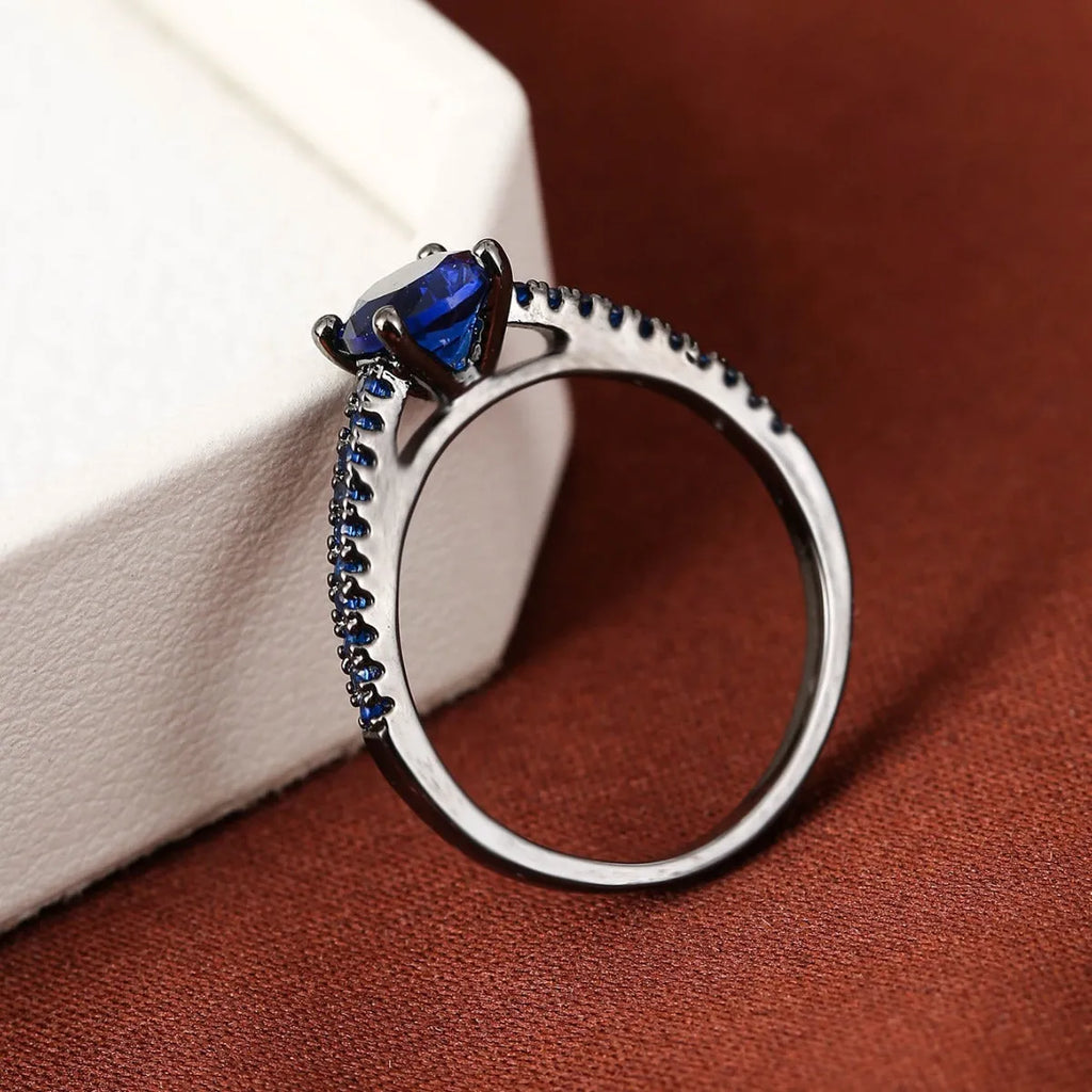 A hexagonal geometric ring with a zircon stone, shown in a gun black and rose red electroplated finish on a finger.