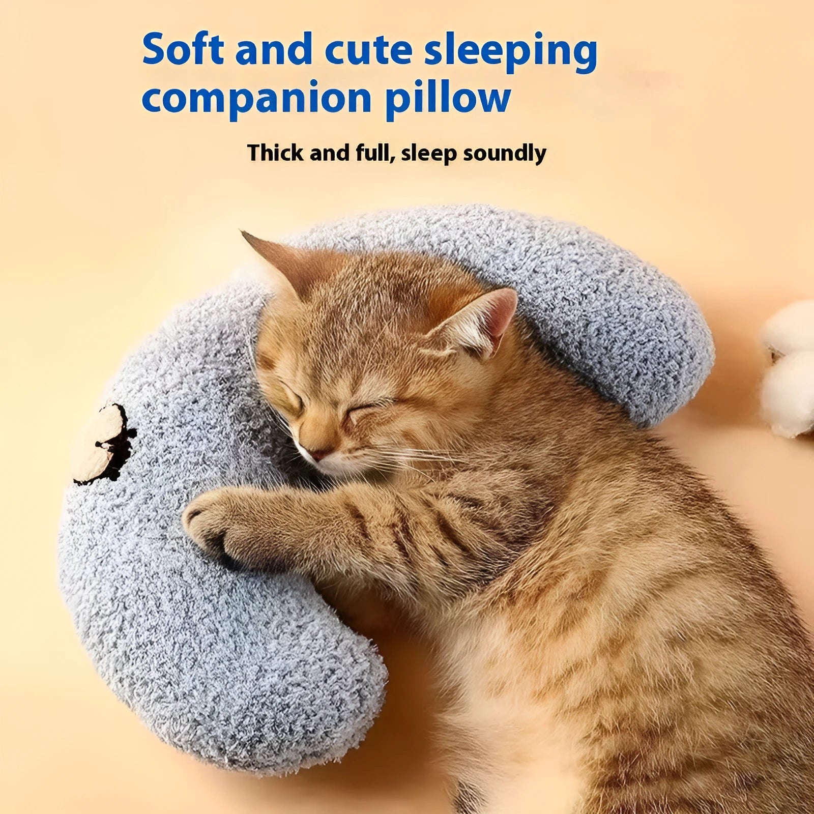 Blue U-shaped cloth pet pillow in a question mark shape on a wooden floor next to a cat carrier.