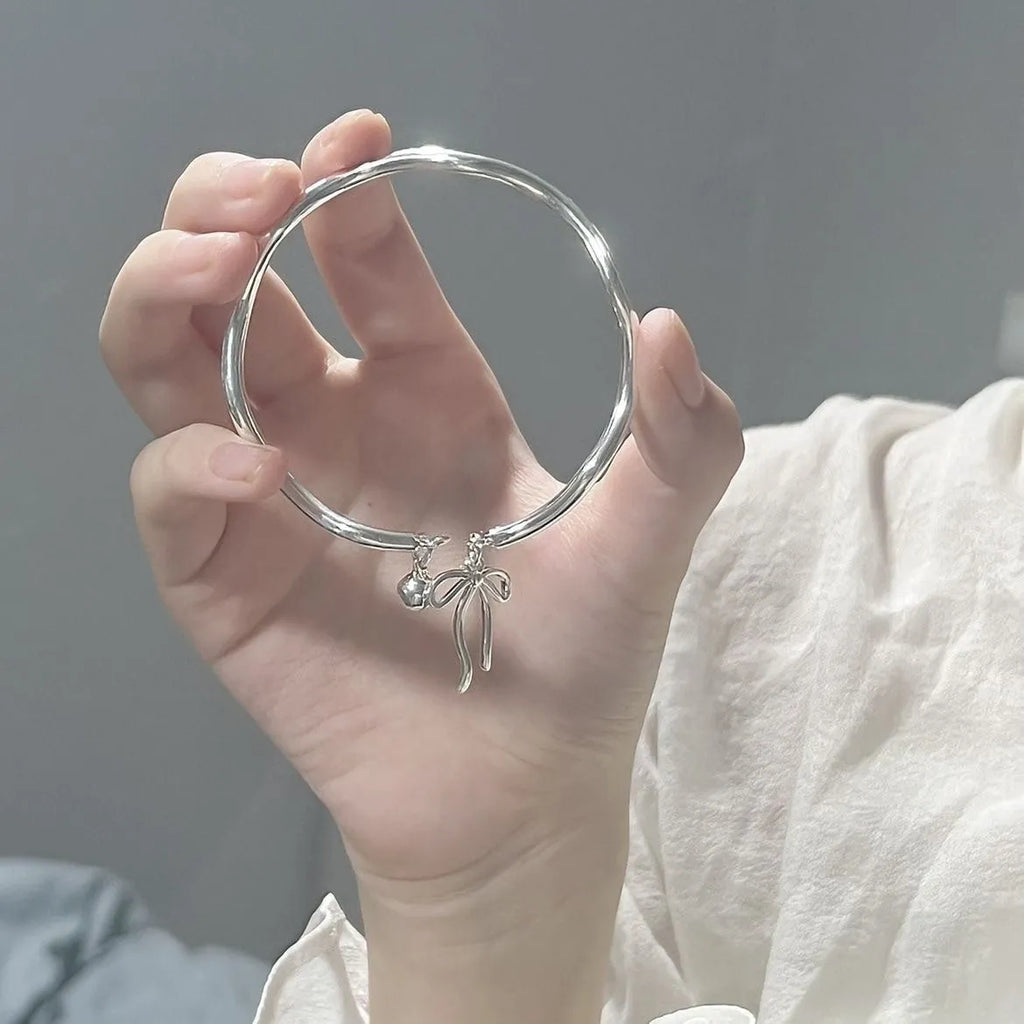 Silver adjustable bracelet with a large bow charm on a model's wrist, showing the sliding clasp.