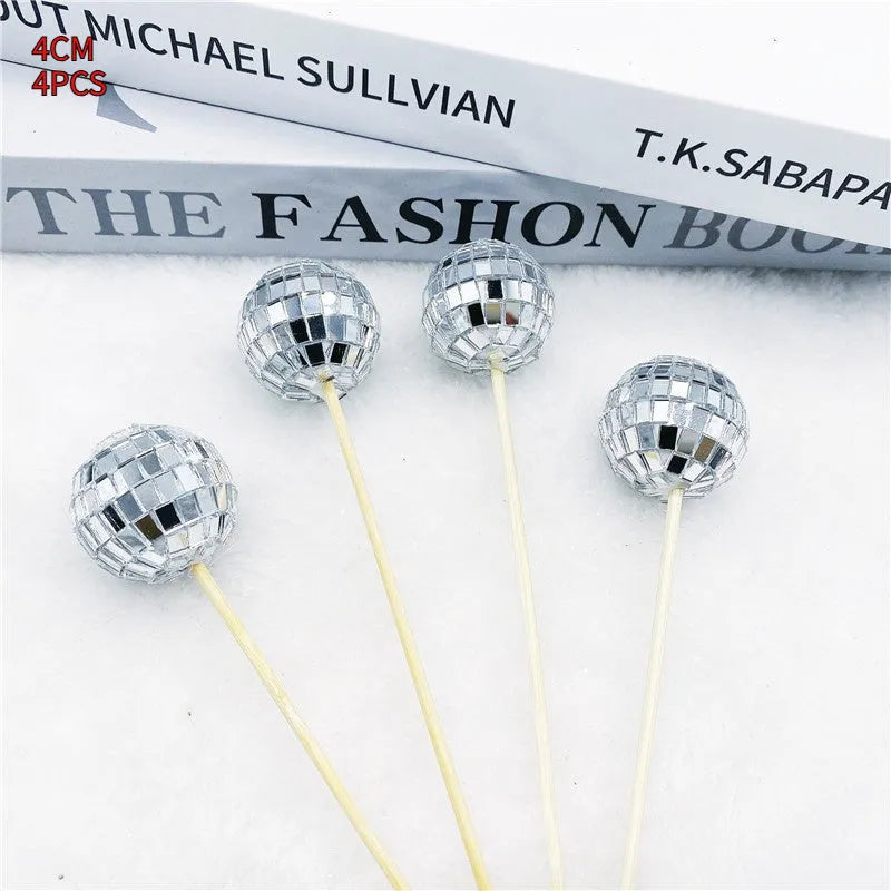 Glass disco ball cake decoration on a wooden stick in various sizes on a cake.
