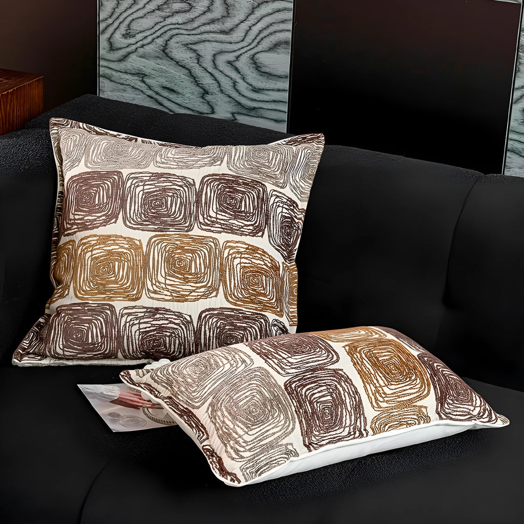 Cream and coffee abstract coil pattern square decorative pillow cover on a grey sofa.
