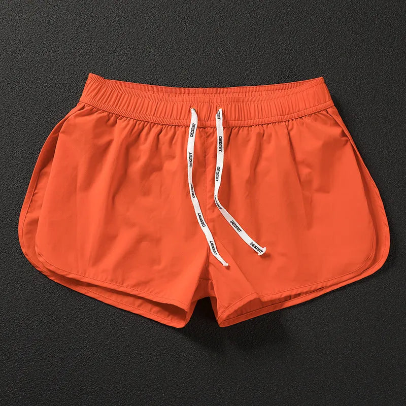 Man wearing loose orange red polyester beach shorts on sand
