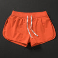 Man wearing loose orange red polyester beach shorts on sand