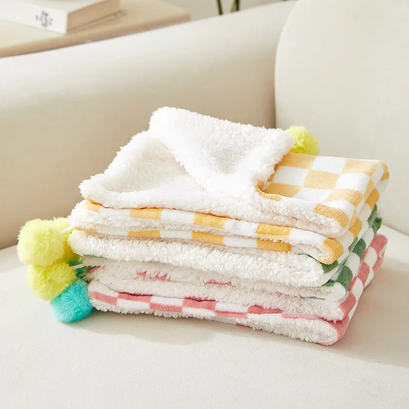 Plush pet blanket with plaid pattern and fur ball decoration for cats and dogs on sofa