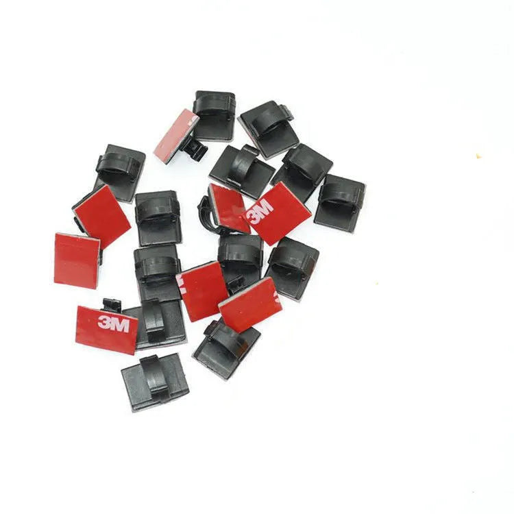 Black and white plastic self-adhesive wire clamps for organising flat cables on a surface.