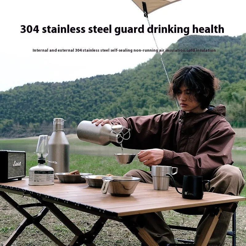 Large stainless steel outdoor thermal pot with a handle, shown in a natural setting.
