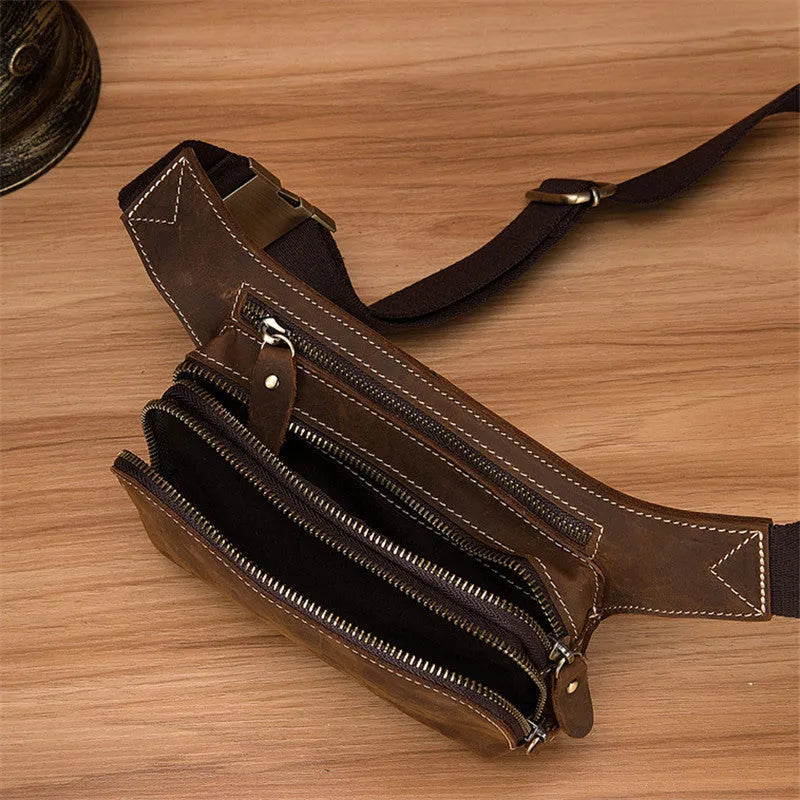 Brown top layer cowhide men's waist bag with pull-cord closure, shown open to reveal internal laptop sleeve and phone pocket.