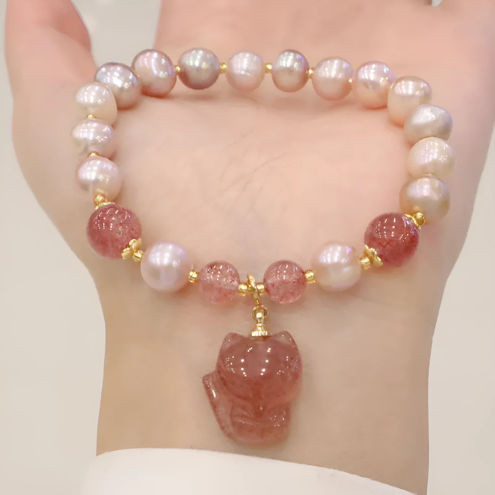 Women's light pink freshwater pearl bracelet with strawberry quartz and fox charm on wrist