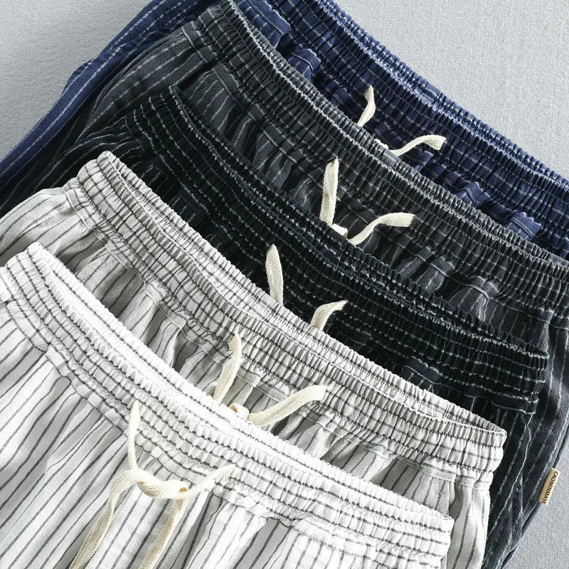 Man wearing loose straight-leg striped cotton shorts in a light colour, showing the mid waist and casual fit.