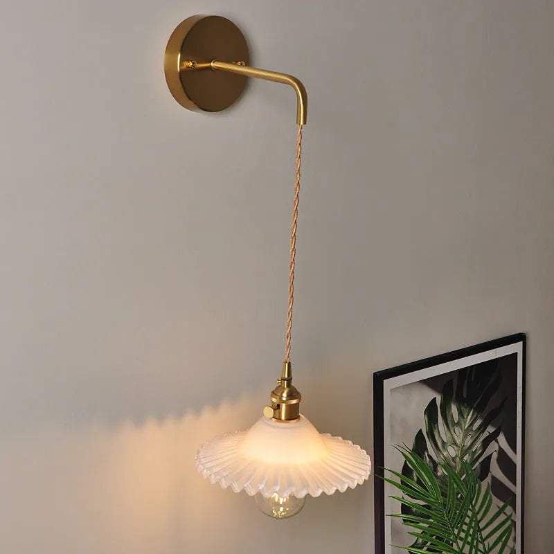 Retro brass lotus wall lamp with a 22cm green glass shade mounted on a copper base beside a bed.