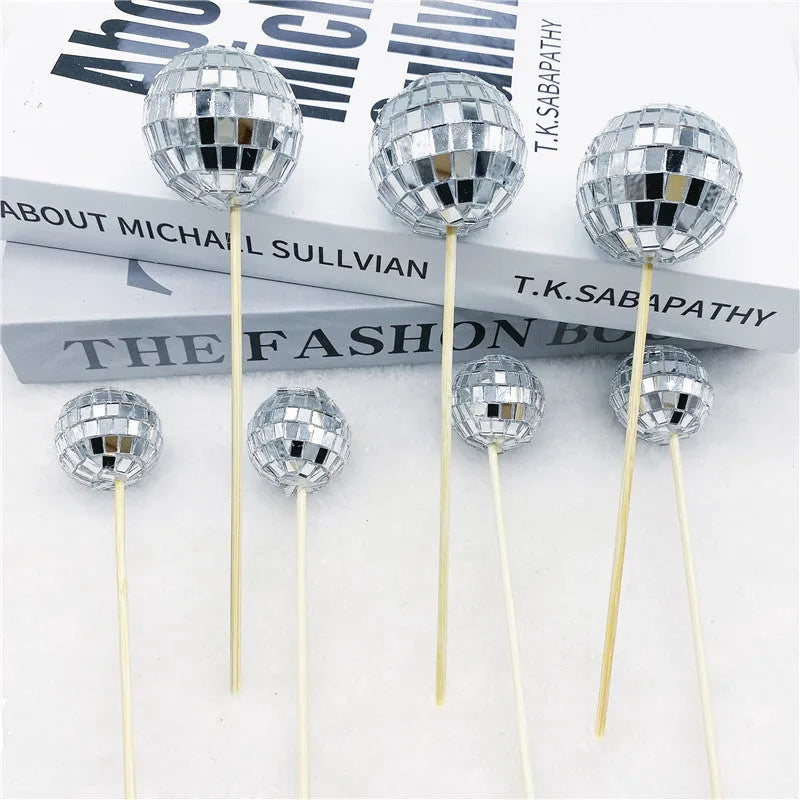 Glass disco ball cake decoration on a wooden stick in various sizes on a cake.