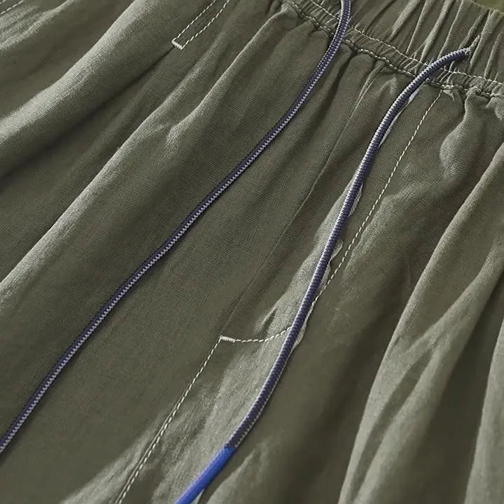Man wearing loose straight-leg linen shorts in green, showcasing mid-waist and drawstring detail.