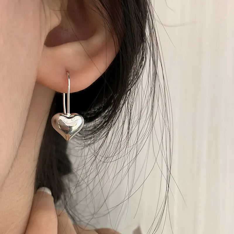 Silver glossy 3D heart-shaped earrings with Korean style hooks on a white background.