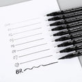 Set of 12 black comic drawing pens with assorted microtip nibs in a fabric organiser pouch.