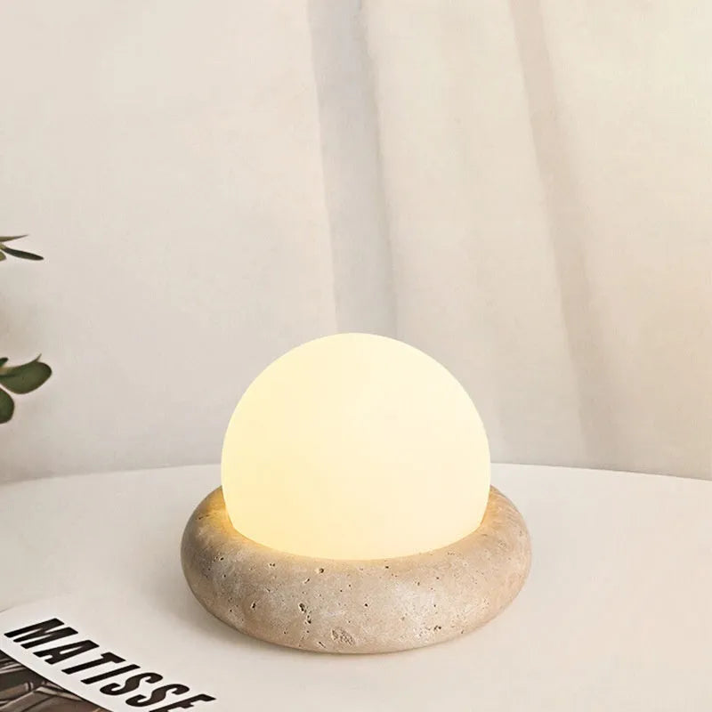 Cream coloured modern bedside night lamp with remote control on a table.