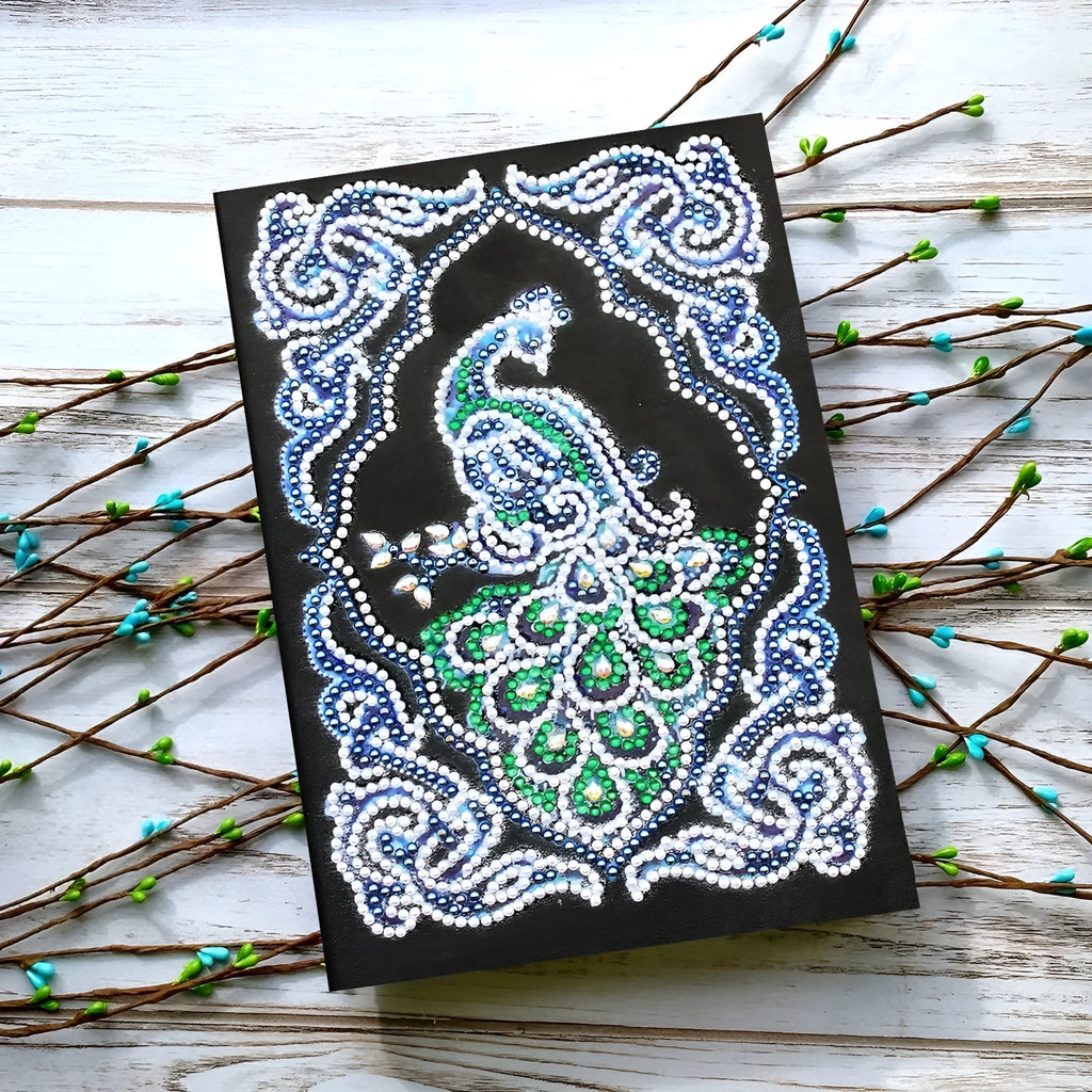 Black A5 hardcover Peacock Beauty journal open showing diamond painting canvas and organised drills in clear OPP bags.