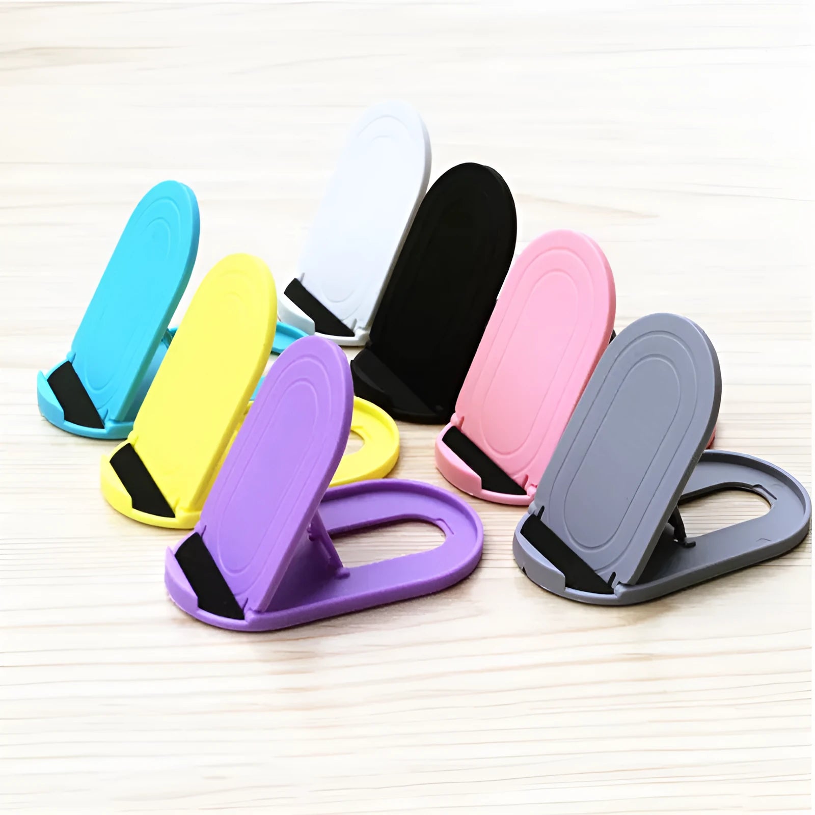 Plastic lazy bracket mobile phone stand in multiple colour choices on a table.