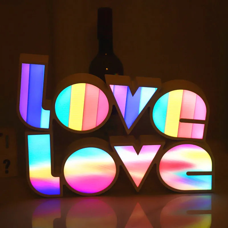 LED LOVE light with rainbow-coloured plastic shade on a desk.