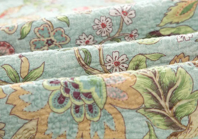 American-style floral quilted cotton bedspread in blue, shown draped on a double bed.