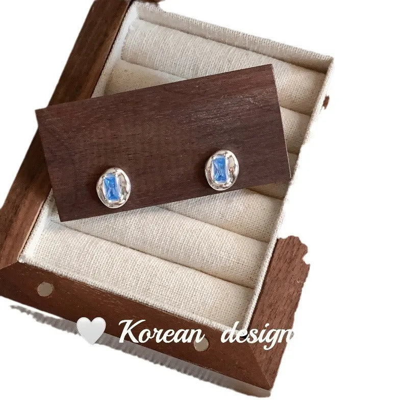 Women's sterling silver earrings with oval heart-wrapped design and blue diamond accents