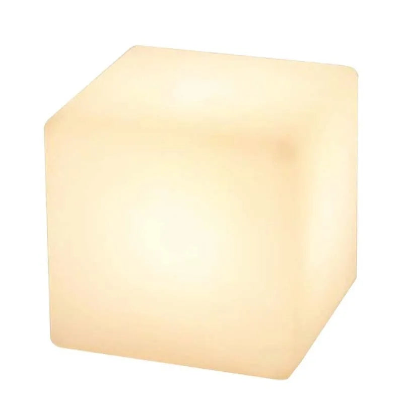 A white square cube LED stool light sitting on a patio, illustrating its modern design and outdoor use.