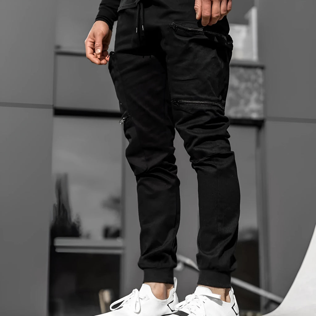 Men's tight fit multi-pocket cotton trousers in black, shown with multiple front pockets and tethered details on waistband.