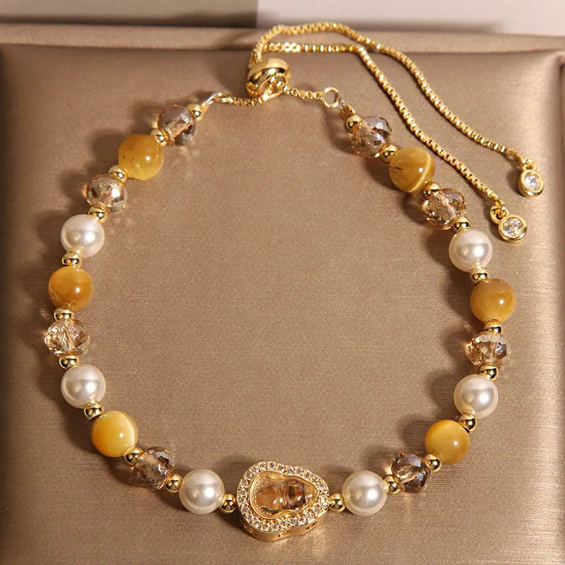 Yellow tiger's eye glass gourd pendant bracelet with alloy inlay and stone accents on a wrist.