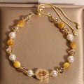 Yellow tiger's eye glass gourd pendant bracelet with alloy inlay and stone accents on a wrist.