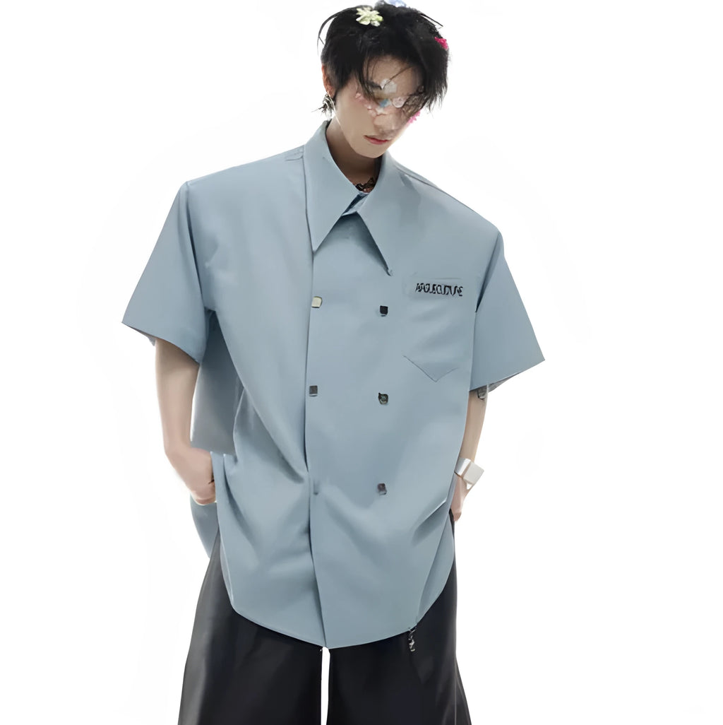 A man wearing a loose-fitting black short-sleeved casual shirt with spliced detailing and metal buttons.