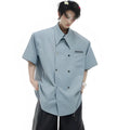 A man wearing a loose-fitting black short-sleeved casual shirt with spliced detailing and metal buttons.