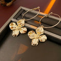 A pair of metal flower geometric earrings with a silver needle post in a gold or silver electroplated finish.