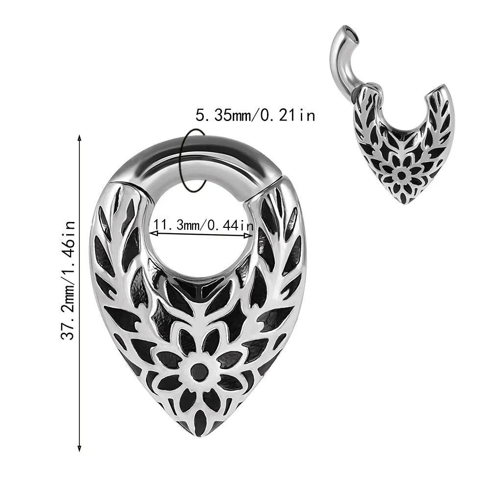 Close-up of a polished silver drop-shaped ear stretcher with a detailed totem pattern, shown against a neutral background.