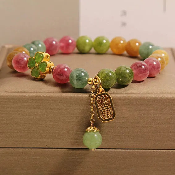 Natural colour tourmaline bracelet with four-leaf clover pearl pendant, geometric drop shape on woman's wrist.