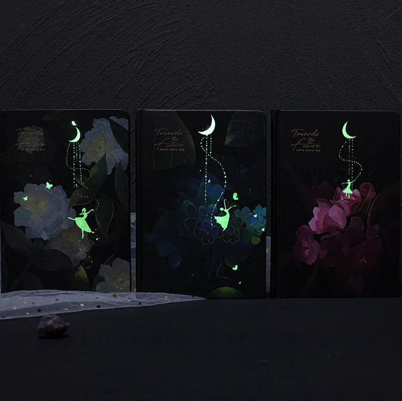 A5 notebook with a luminous cover shown in deep blue, open to reveal pages with colour illustrations.