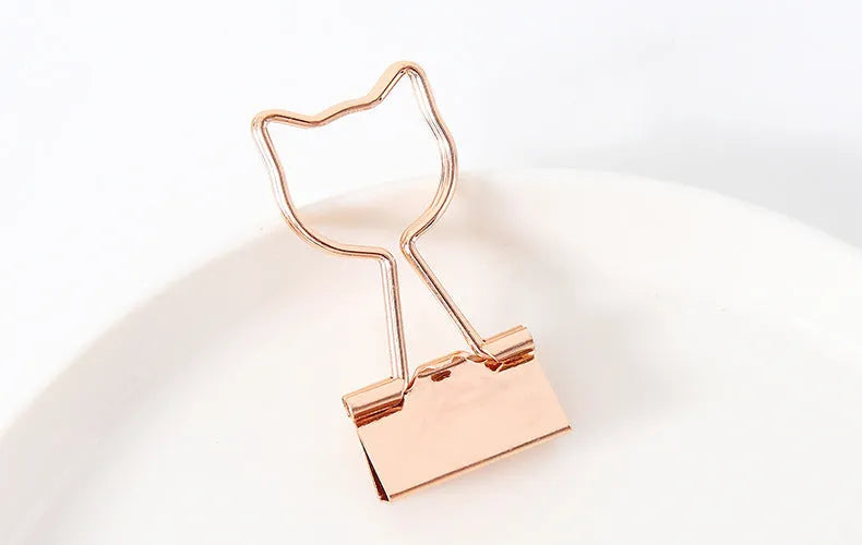 Gold metal paper clip with a long tail, showing decorative flamingo, love, cloud, cat, cactus, and bow motif options.